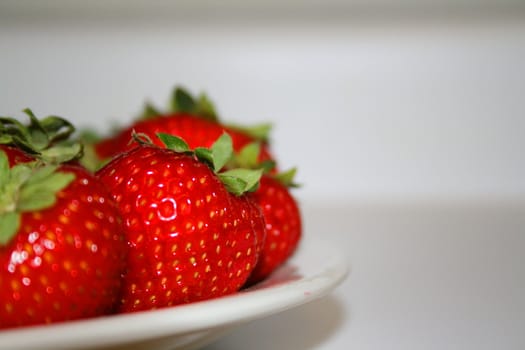 Close up of ripe strawberries on a plate with a white background.
