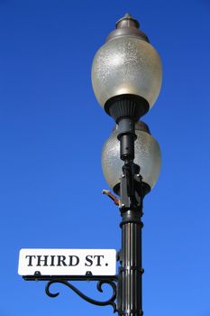 Street sign on a light pole over blue sky.
