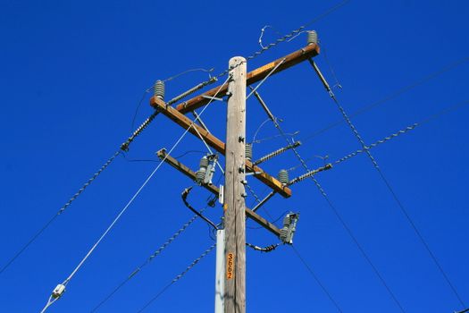 Close up of a telephone pole over blue sky.
