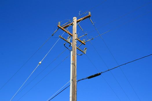 Close up of a telephone pole over blue sky.
