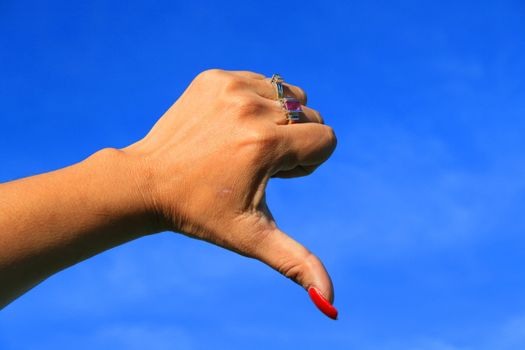 Woman's hand showing thumb down sign over blue sky.