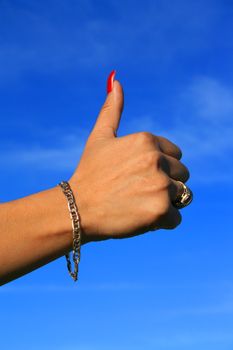 Woman's hand showing thumb up sign over blue sky.