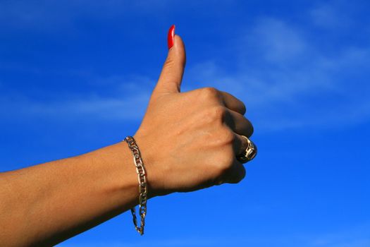 Woman's hand showing thumb up sign over blue sky.