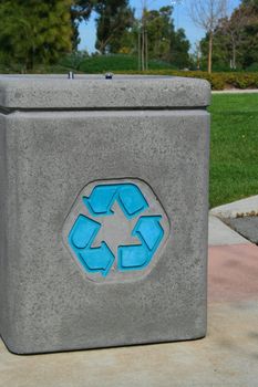 Recycle can on a sidewalk in a park.
