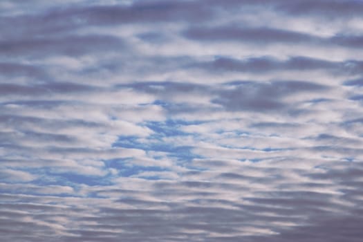 blue sky striped with white and grey clouds with small openings between them