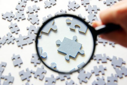 Hand with magnifying glass and puzzle isolated on white background