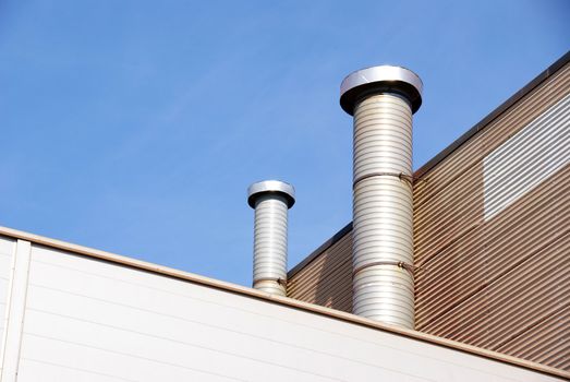 Pipes of ventilation are located on a wall of an industrial building