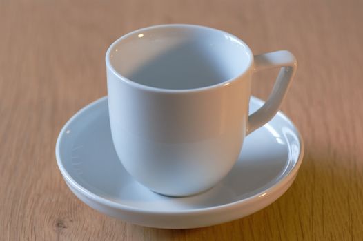 A white cup and saucer on an oak table top