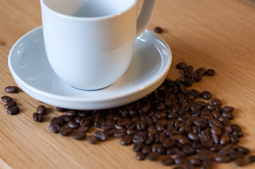 A white coffee cup and saucer on an oak table with coffee beans