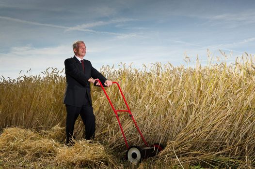 Seniot executive businessman pausing during the challenge of harvesting a field of ripe wheat with a hand lawnmower as he visualises the rewards to be gained at the completion of his task