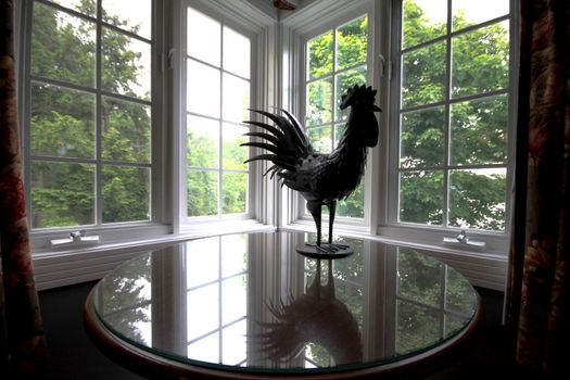 Metallic rooster reflected on a glass table in rustic surrounding