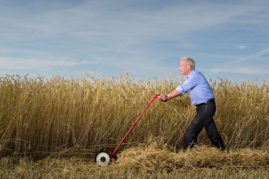 A senior executive businessman strides through a field of ripe grain pushing a manual lawnmower as he harvests and reaps the rewards of all his hard work and business planning