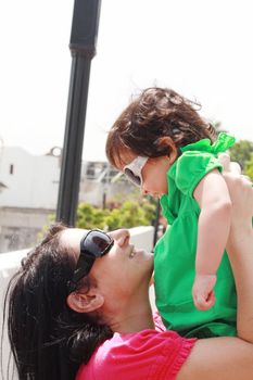 beautiful little and happy daughter smiling with her head against head of her mother. Summer park in background.