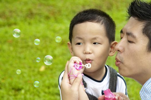 Asian father and son blowing bubbles outdoor