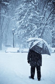 lonely old man with umbrella walking under the snow, selenium toned