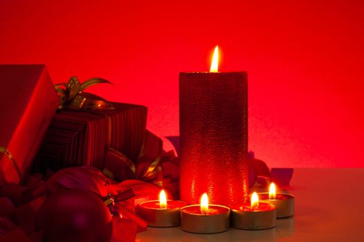 Christmas gifts and candles over red background