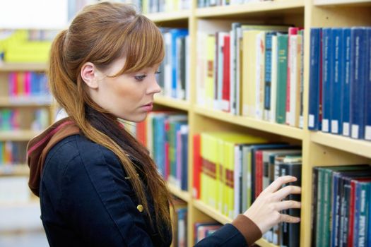 Teenage girl picking up book in library