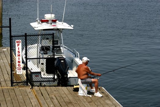 Man fishing on pier next to NO FISHING sign