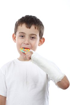 Boy with broken hand in cast, holding a lollipop over white 