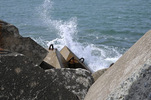 Little wave splashing on concrete blocks with a blue sea