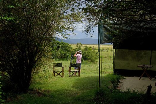 Woman using binoculars by safari tent on Masai Mara