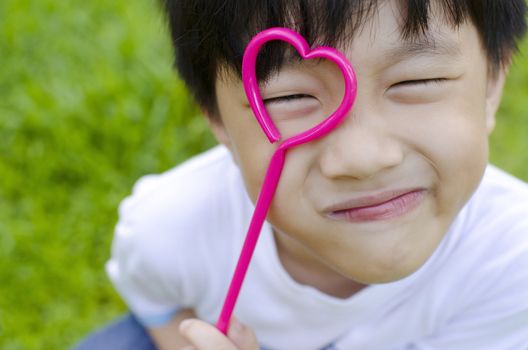 Cute Asian boy holding a heart shape on his eye