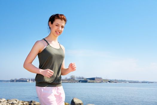 Teenage girl jogging by sea looking at camera