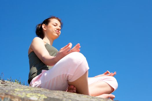 Teenage girl meditating on rock eyes closed