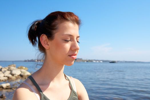 Teenage girl sitting by sea on sunny day eyes closed