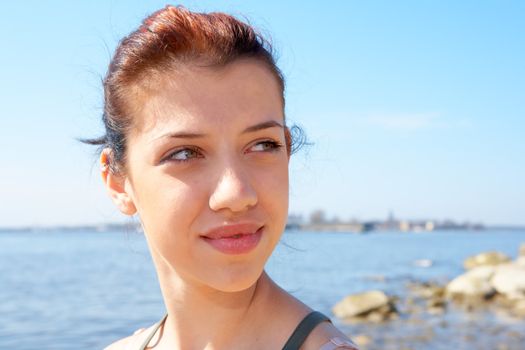 Teenage girl sitting by sea on sunny day contemplating