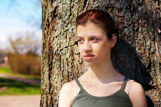 Sad teenage girl leaning to tree in park