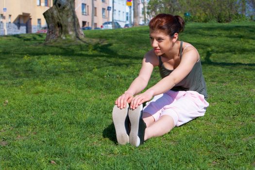 Teenage girl stretching in park, looking away
