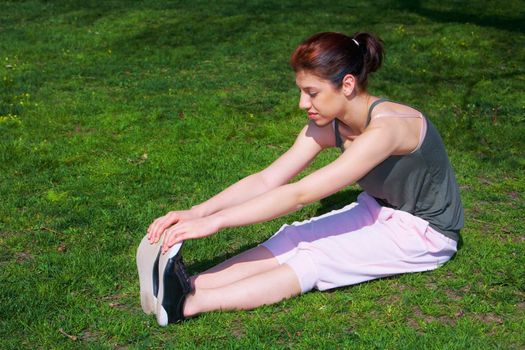 Teenage girl stretching in park, side view