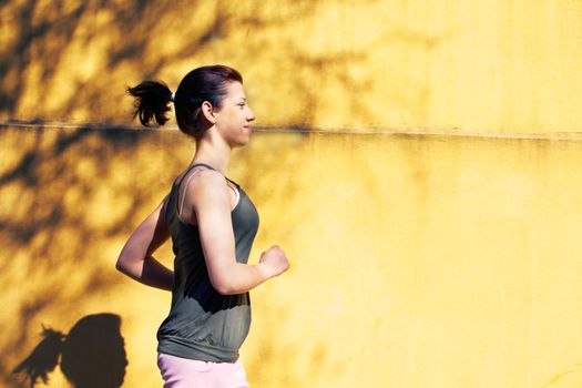 Teenage girl jogging on sidewalk by wall in city