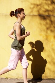 Teenage girl jogging by wall in city