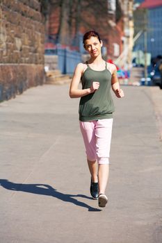 Teenage girl jogging on sidewalk in city, looking at camera