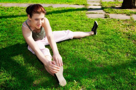 Teenage girl stretching on park grass in spring