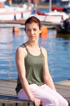 Teenage girl sitting in harbor, boats in background