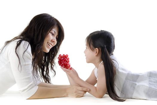 Mother and daughter sharing grapes on white background