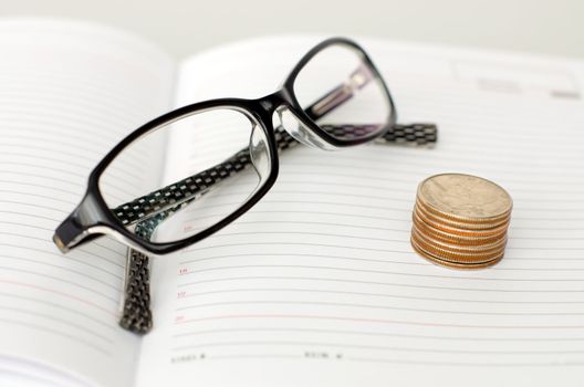 Business glasses, diary and piles of coins