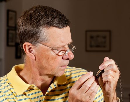 Senior repairing an old pocket watch with screwdriver and wearing very strong lens glasses to magnify the mechanism