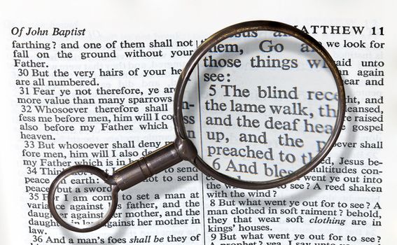 Antique brass magnifying glass over the top of an Authorized King James Bible on the paragraph about blind being able to see