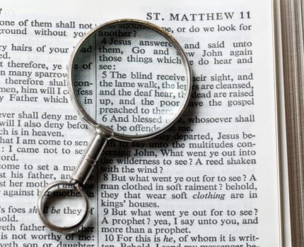 Antique brass magnifying glass over the top of an Authorized King James Bible on the paragraph about blind being able to see
