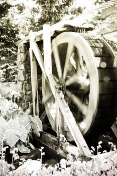 an antic water wheel running in a garden, faded colour