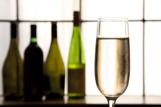 Glass of champagne in foreground with sepia tones and bottles in back ground.