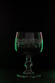 a glass  lighted up with green and violet color on the black background.