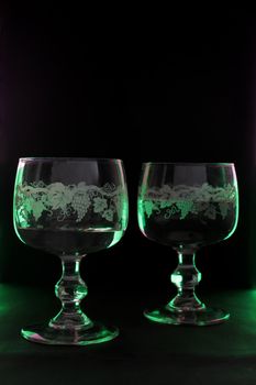 two goblets lighted up with green and violet color on the black background.