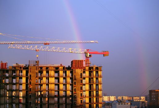 The elevating crane of construction on a background of the dark blue sky and a rainbow