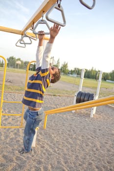 young kid playing at the playground stretching his hands to hang on the next bar