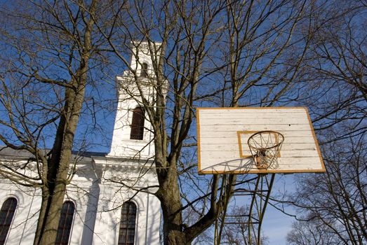 Old basketball board with an old tattered basketball net on the hoop near church.